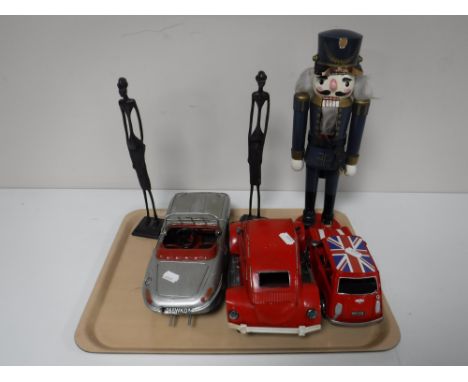 A tray containing two metal tribal figures, a wooden nut cracker figure and three tin cars 