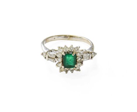 An Emerald and Diamond Cluster Ring, the rectangular step-cut emerald within a border of round brilliant cut diamonds, in whi