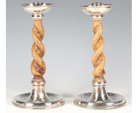 A pair of George V Arts and Crafts silver mounted oak barley twist candlesticks, each cylindrical sconce and circular drip pa