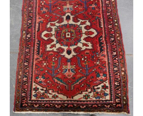 A Hamadan runner, North-west Persia, mid-20th century, the red field with a column of medallions, within a flowering vine bor