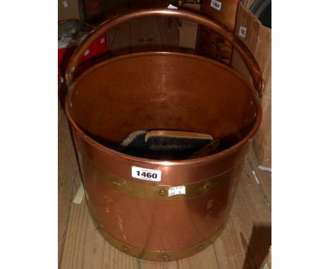 A copper coal bucket with brass banding containing a selection of vintage clothes brushes