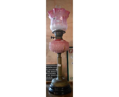 A Victorian double burner oil lamp with moulded opaque pink glass reservoir on brass column stand with ceramic base and etche