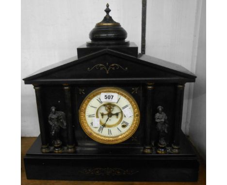 A late Victorian black slate cased mantel clock of architectural design with flanking pillars and figures, visible escapement