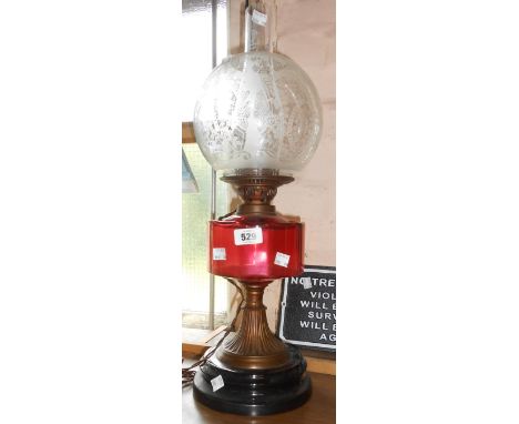 A Victorian table oil lamp with ruby glass reservoir, flared brass column and ceramic base with etched globe glass shade - co