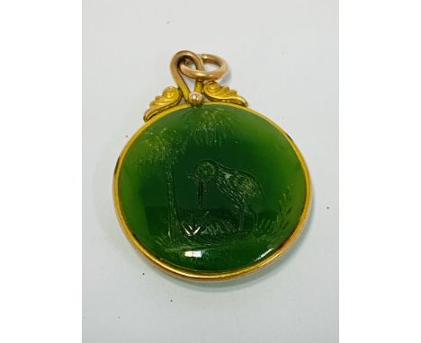 An unmarked gold mounted nephrite jade pendant with hand carved image of a Kiwi and palm tree. (2cm diameter).