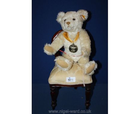 A cream Steiff bear with button in the ear, wearing a Millennium medal, sat on a Teddy bear chair