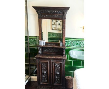 A narrow Victorian carved oak mirror backed cabinet, the pediment above a carved frieze flanked by lion masks with bevelled m
