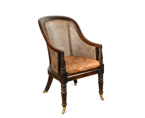 A mahogany caned bergere armchair, 19th century, with shaped back, buttoned brown leather squab seat cushion, on turned front