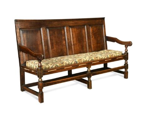An oak panel backed settle, 18th century, with four fielded panels above a loose rectangular cushion upholstered in crewel ty