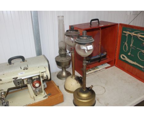 An oil lamp with glass chimney together with two paraffin pressure lamps