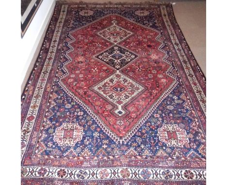 *Carpet. An Oriental woollen carpet with three central diamonds on a red and blue ground within multi banded border,  315 cm 