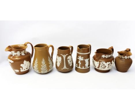 A collection of six Dudson or Spode brown jugs, all with white relief designs of foliage, figures and others. Only one stampe