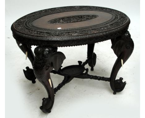 A profusely carved oval Indian occasional table raise on four elephant trunk supports united by a cross stretcher.