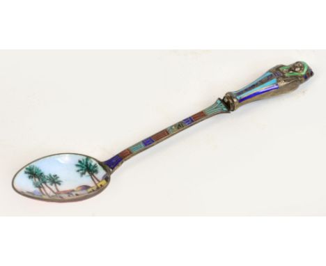 An unusual white metal and enamel decorated spoon of Egyptian design, the bowl enamel decorated with a landscape, the termina