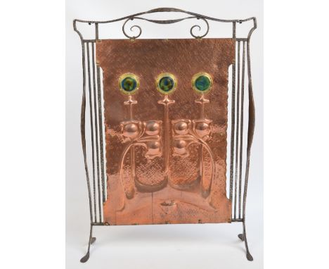 An Art Nouveau wrought iron framed fire screen with embossed copper panel decorated with stylised floral motifs set with thre