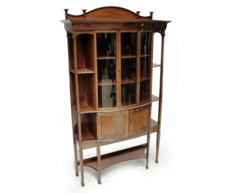 An Art Nouveau mahogany display cabinet of bowfront outline, the glazed upper section above two cupboard doors flanked by ope