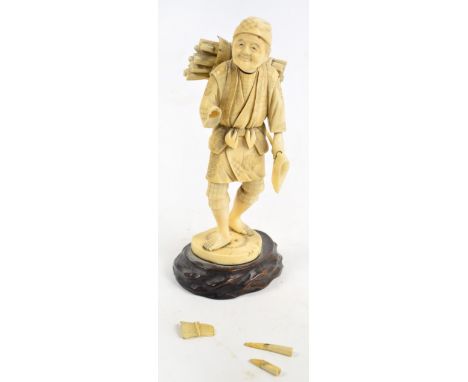 A Japanese Meiji period ivory okimono of a woodcutter with a roll of logs on his back, and carrying an axe in his left hand, 