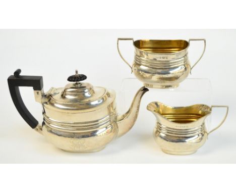 An Edward VII hallmarked silver three piece tea service comprising a teapot of oval form, a twin handled sugar bowl with gilt
