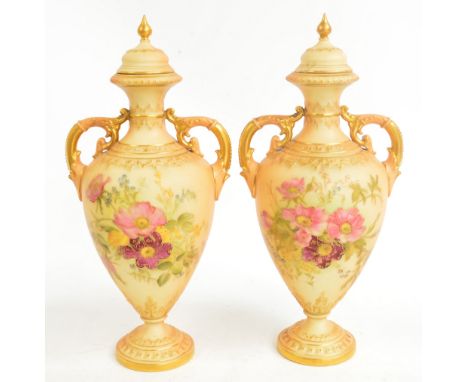 A pair of Royal Worcester twin handled vases with finialled lids, with gilt heightened floral painted decoration, raised on c