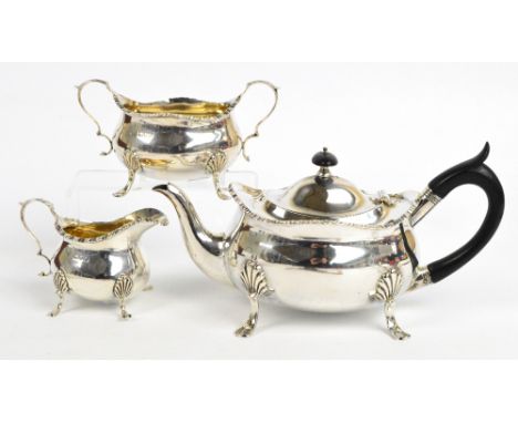 An Edward VII hallmarked silver three piece tea service comprising a teapot of oval form with raised cast decorated rim, rais