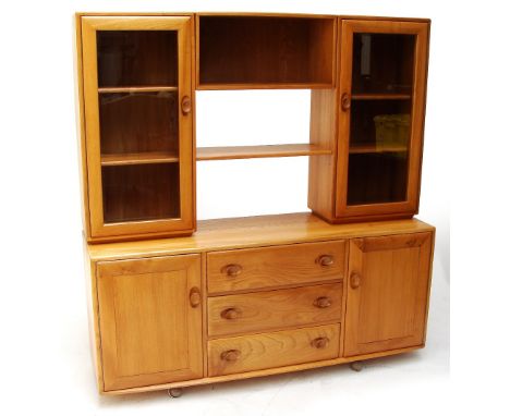 A 1970's Ercol Windsor blonde elm sideboard with three central drawers flanked by a pair of hinged cupboards enclosing shelve