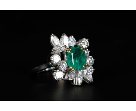 AN EMERALD AND DIAMOND CLUSTER RING, c.1965, claw set to the centre with a step-cut emerald raised against a random cluster o