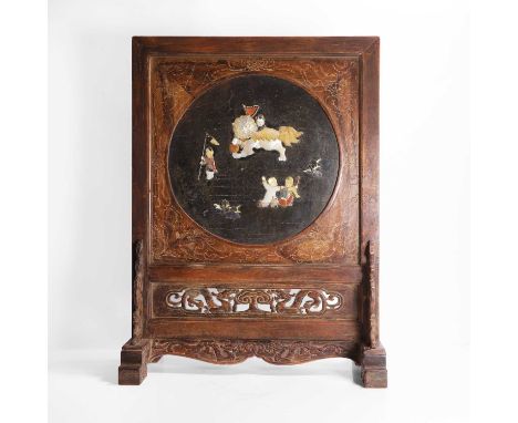 A Chinese hardwood table screen, inset with a circular black-lacquered panel onlaid with boys playing with a Buddhist lion in
