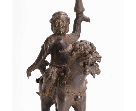 A Chinese bronze candlestick, Ming dynasty (1368-1644), in the form of a foreigner seated on the back of a Buddhist lion, his
