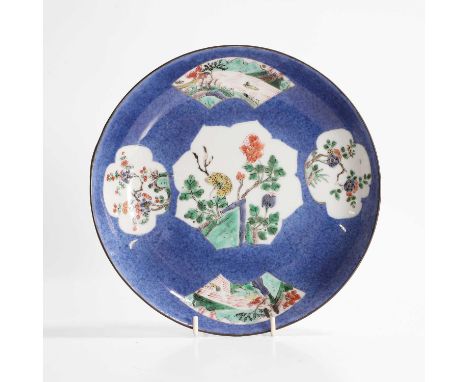 A Chinese famille verte plate, Kangxi (1662-1722), of circular form, painted with landscapes or flowers by rocks in shaped pa