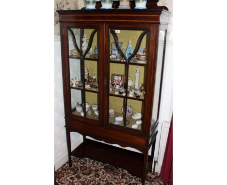 Edwardian inlaid mahogany display cabinet with ledge back above twin astragal glazed doors with shelf below, on square taper 