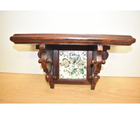 A solid mahogany bracket in the Aesthetic style, the centre tile decorated with foliage on a cream ground, w44cm.