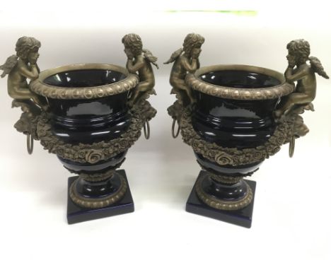 A pair of ceramic urns with decorative metal fittings in the form of cherubs and floral swags, approx height 35cm.