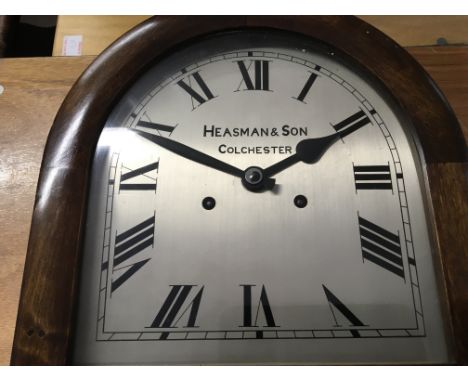 An Early 20th century wall clock with an arched silvered dial maker Heasman &amp; Son Colchester. Length 72cm