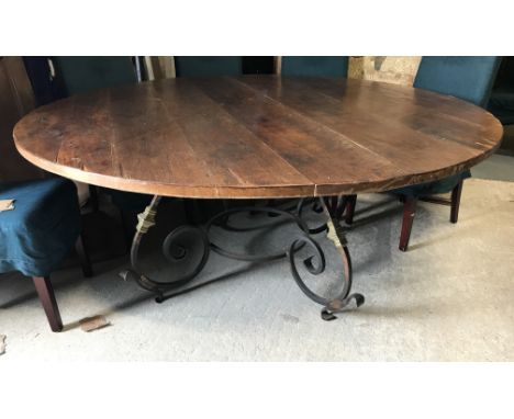 A modern oak dining table, the circular plank top on a blackened and gold painted iron scrollwork base, 184 cm wide x 77 cm h