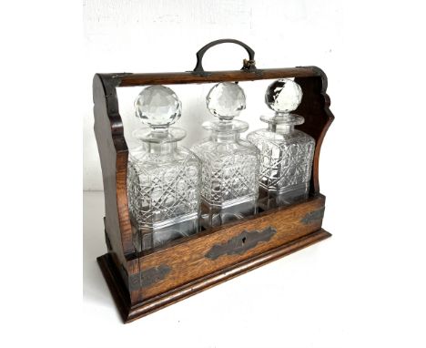 An early 20th century oak three-bottle Tantalus - with the three original decanters and key, 30 cm high, 34.7 cm long.