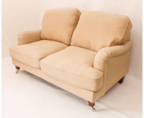 A modern two-seater sofa - upholstered in pale biscuit-coloured fabric with loose back and seat cushions, the zipped cushion 