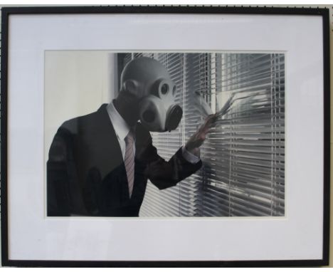 A late 20th century photographic print of a businessman wearing a respirator, peering through a blind. 39 x 57cm