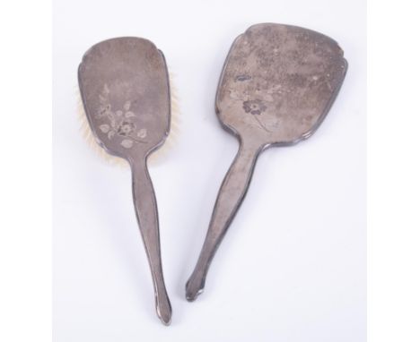 A matching silver backed dressing table mirror and brush, decorated with a flower.