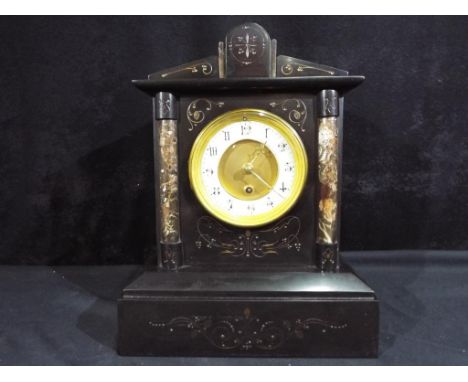 A French black marble mantel clock of architectural form flanked by contrasting lighter marble columns, incised, gilded decor
