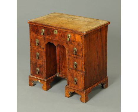An 18th century walnut veneered kneehole desk, with crossbanded top with reentrant corners above a series of frieze drawers a