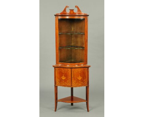 An Edwardian inlaid mahogany serpentine fronted corner cupboard, with swans neck pediment above a glazed door enclosing shelv