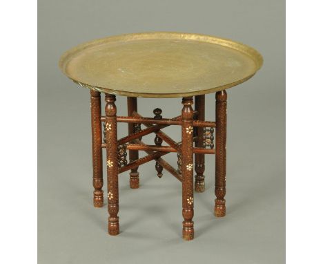 An Eastern brass topped table, decorated with Islamic script and raised on a mother of pearl inlaid folding stand.  Diameter 