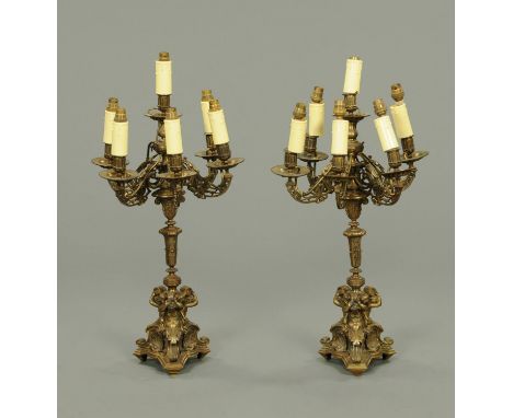 A pair of brass six branch candelabra, fitted for electricity, in the Classical style and raised on triform bases.  Height to