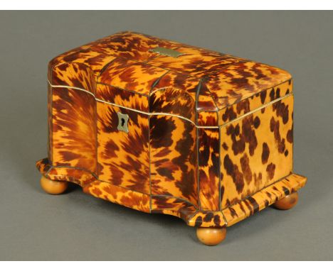 An early 19th century tortoiseshell tea caddy, shaped outline, with two interior compartments and raised on ball feet.  Width