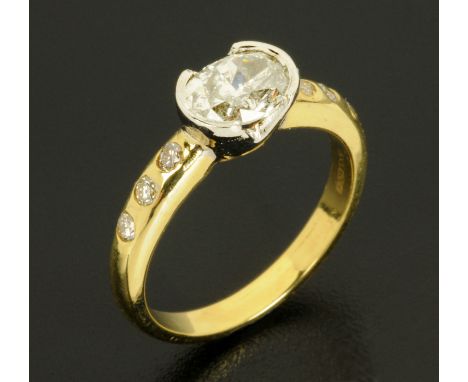 An 18 ct gold two tone diamond set ring, rubover, with oval diamond to centre and diamond set shoulders, total diamond weight