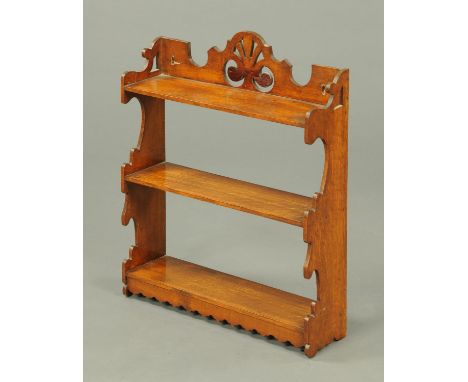 An Edwardian oak three tier open hanging shelf unit, with pierced pediment and sides of shaped outline.  Width 54.5 cm. 