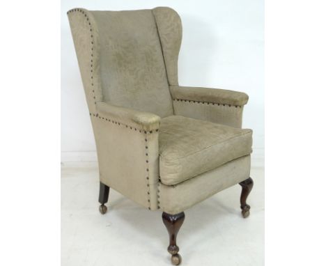 An Edwardian wing armchair, with cabriole front legs, upholstered in cream fabric with foliate brocade and studded edging, on