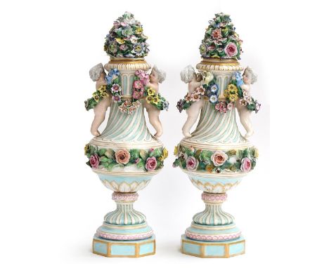 A pair of 20th Century porcelain vases, each with flower-encrusted cover, the fluted urn-shaped bodies with applied cherubs a