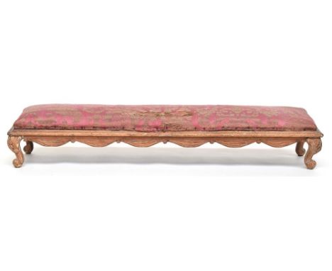 A Louis XVI style fruitwood long upholstered footstool, with swag frieze, on short carved cabriole legs with ball feetProvena