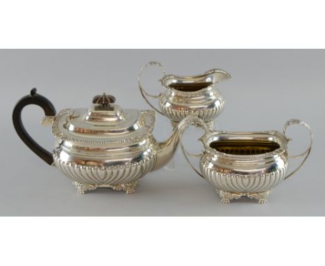 George V silver three piece tea service comprising teapot, cream jug and sugar bowl, with half-gadrooned bodies and foliate s